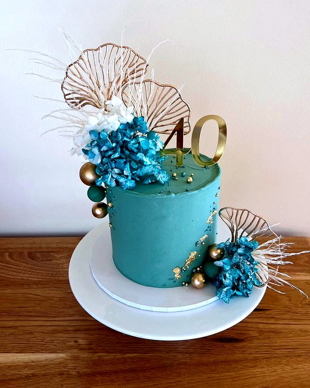 An emerald buttercream cake with dried blue hydrangea, gold wire leaves, gold leaf and a gold 40 topper.