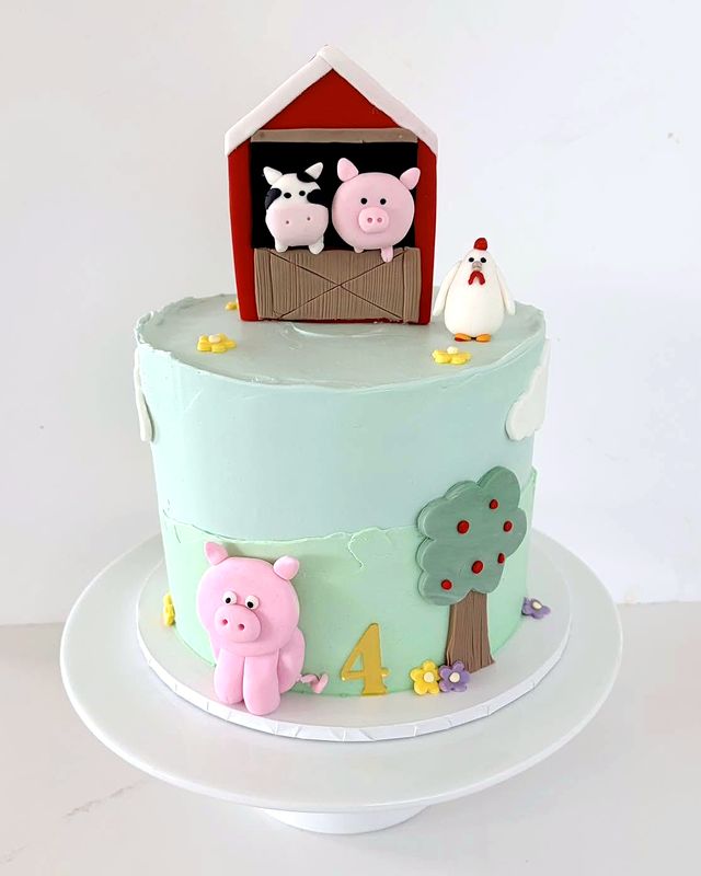 A mint green cake with a cow and a pig in a red barn on top, a pink pig, a hen, an apple tree and a gold 4.